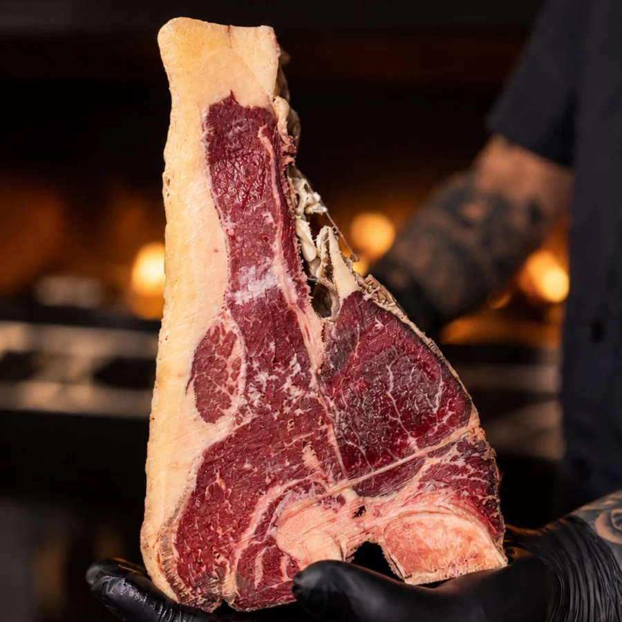T-Bone madurado en seco, sostenido frente a la parrilla antes de cocinarse
